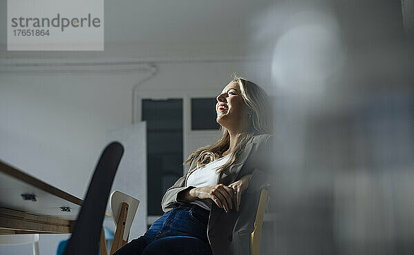 Glückliche Geschäftsfrau sitzt auf einem Stuhl im Konferenzraum im Büro