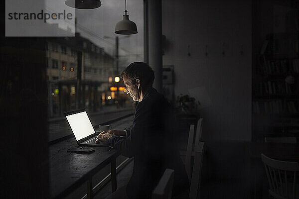 Geschäftsmann arbeitet im Dunkeln im Café am Laptop