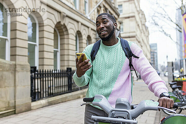 Mann steht mit Elektrofahrrad und hält Smartphone in der Hand