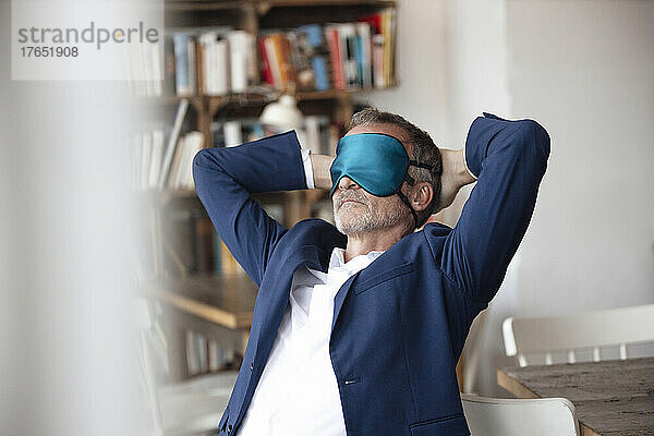 Businessman with eye mask sitting with hands behind head at cafe