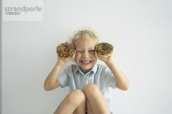 Glückliches Mädchen mit Donuts  das vor der Wand sitzt