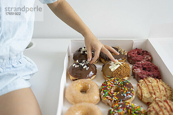Hand eines Mädchens mit Schokoladenüberzug auf Donuts in einer Schachtel