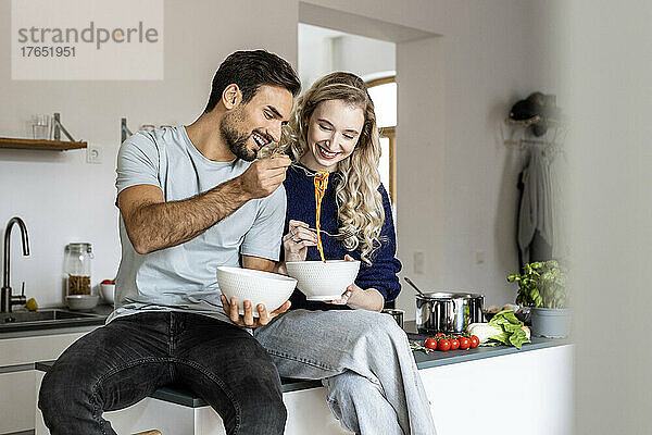 Glückliches Paar isst Nudeln und sitzt zu Hause auf der Küchentheke