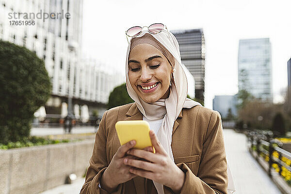 Glückliche junge Frau  die im Büropark Textnachrichten per Smartphone sendet