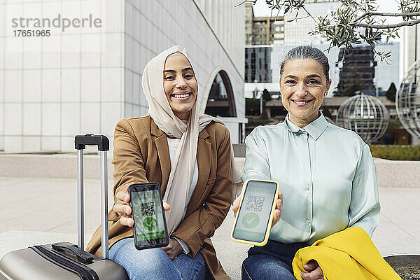 Lächelnde Geschäftsfrauen zeigen auf Mobiltelefonen das Impf-QR-Zertifikat