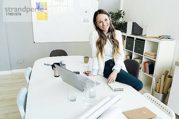 Lächelnde Geschäftsfrau mit Laptop am Schreibtisch im Büro