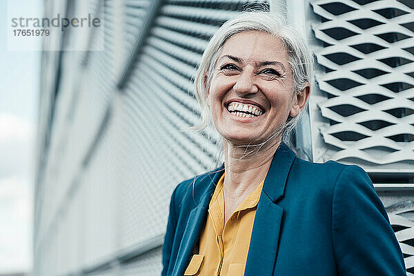 Businesswoman with gray hair laughing in front of wall