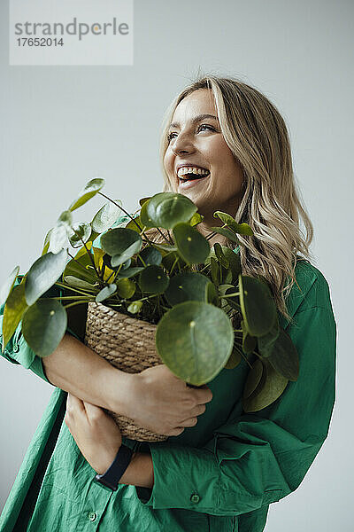 Fröhliche Frau hält Zimmerpflanze vor weißem Hintergrund