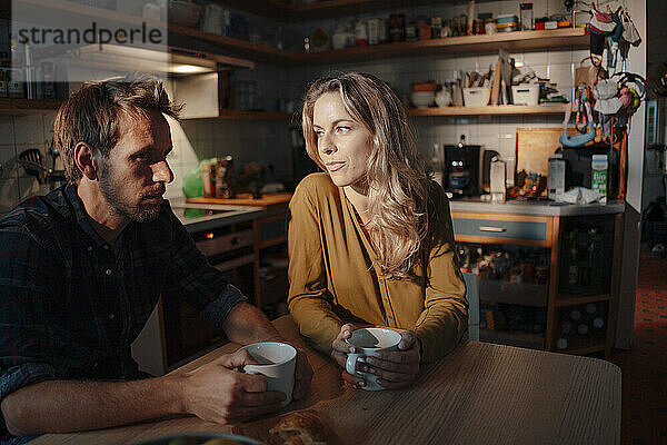 Mann und Frau sitzen mit Kaffeetassen am Tisch in der Küche