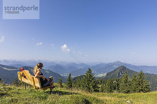 Deutschland  Bayern  Wanderin entspannt auf einer Bank am Gipfel des Fockensteins