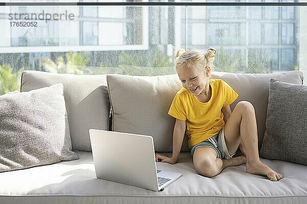 Glückliches Mädchen  das auf dem Sofa sitzt und auf den Laptop schaut