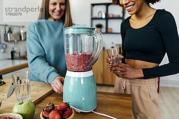 Glückliche Frau  die zu Hause in der Küche Smoothie zubereitet