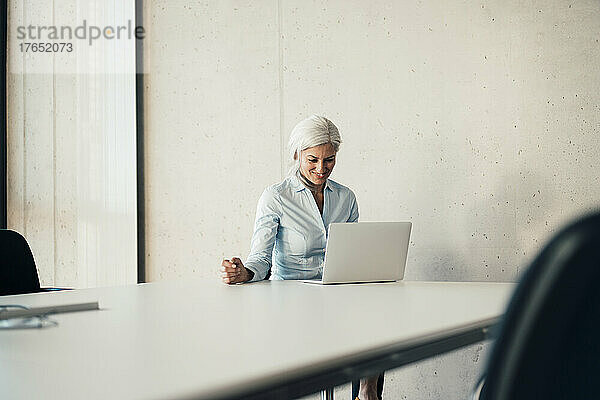 Lächelnde berufstätige Frau mit Laptop am Schreibtisch im Büro
