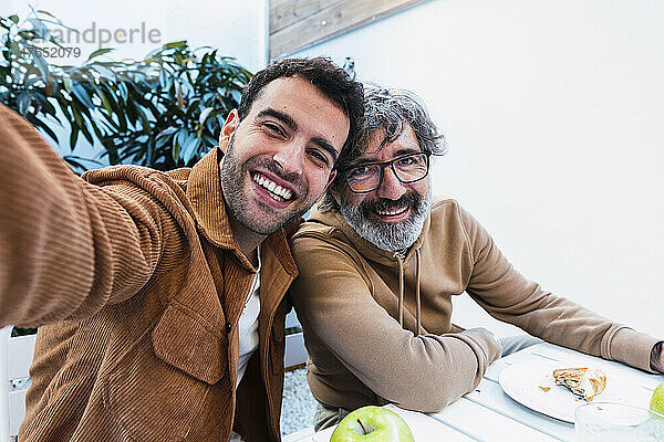 Glücklicher Vater und Sohn machen Selfie und frühstücken gemeinsam