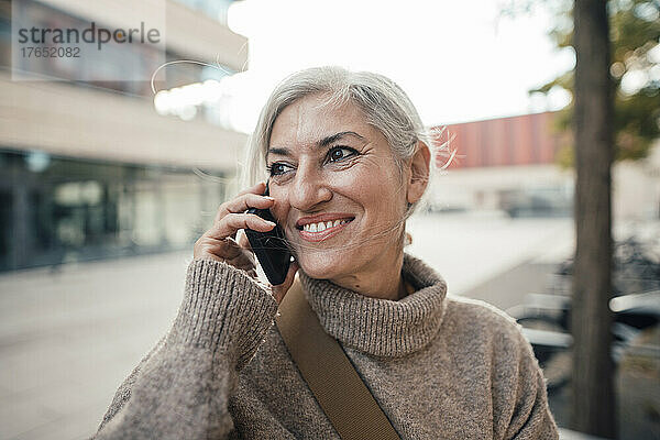 Lächelnde Geschäftsfrau  die im Büropark mit dem Mobiltelefon spricht
