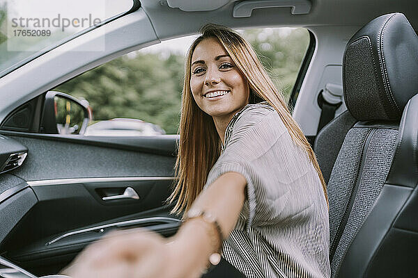 Glückliche blonde Frau hält Händchen und sitzt auf dem Beifahrersitz im Auto