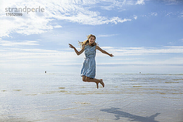 Mädchen springt an einem sonnigen Tag am Strand