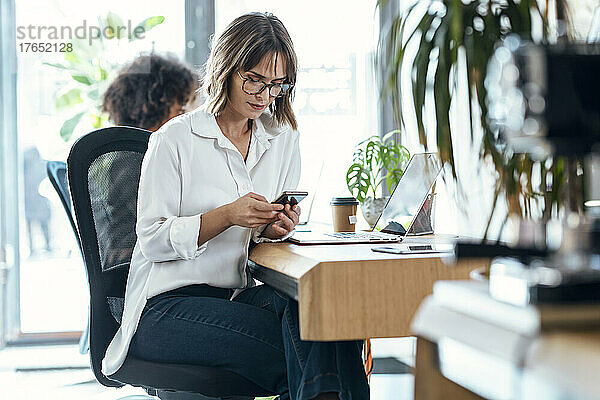 Geschäftsfrau sitzt am Schreibtisch im Büro und nutzt ihr Smartphone