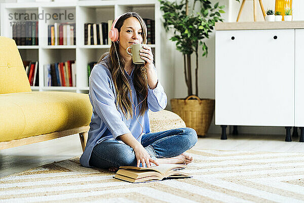 Frau trinkt Kaffee und sitzt zu Hause mit einem Buch auf dem Teppich