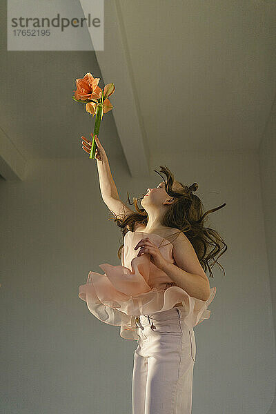 Girl holding flower and jumping in front of white wall