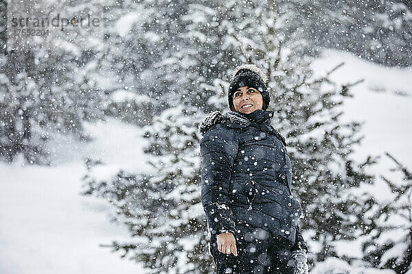 Lächelnde Frau mit Strickmütze genießt den Schneefall