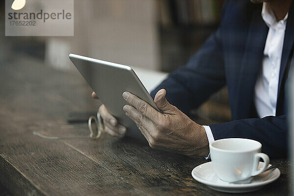 Geschäftsmann mit Kaffeetasse und Tablet-PC sitzt am Tisch im Café