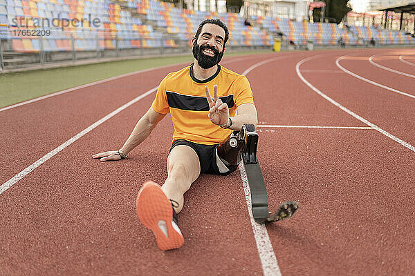 Lächelnder Mann mit Beinprothese sitzt auf der Laufstrecke und zeigt ein Friedenszeichen