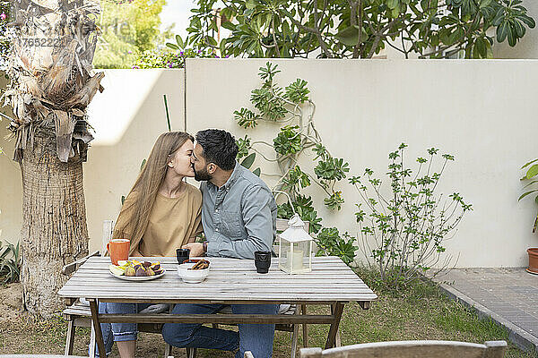 Affectionate couple kissing sitting at table in back yard