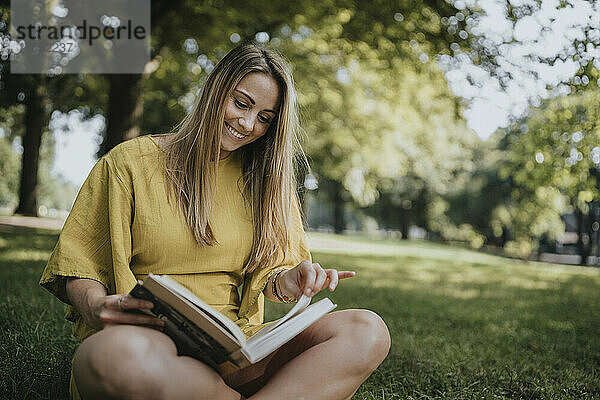 Smiling woman reading book sitting in grass in park
