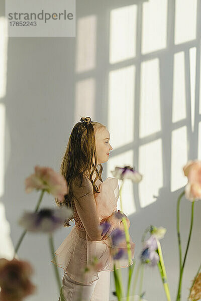 Lächelndes Mädchen  das hinter Blumen an einer weißen Wand steht