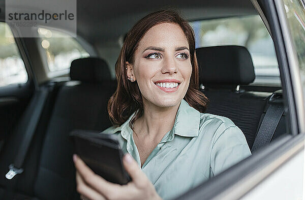 Lächelnde Geschäftsfrau mit Smartphone im Auto sitzend