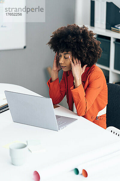 Gestresste Geschäftsfrau mit Kopf in den Händen sitzt mit Laptop am Schreibtisch