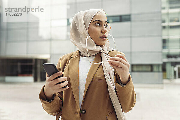 Junge Frau mit Smartphone und Sonnenbrille vor modernem Gebäude