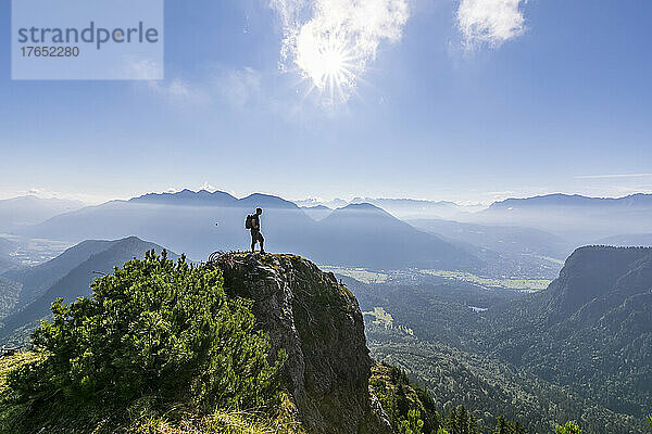 Mann steht an einem sonnigen Tag auf dem Gipfel des Berges
