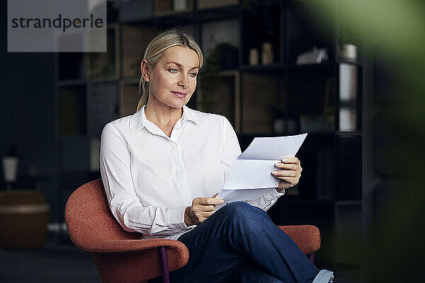 Geschäftsfrau analysiert Dokument auf Stuhl im Büro sitzend