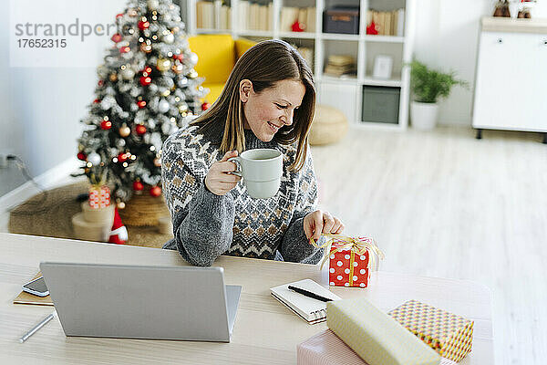 Lächelnde Frau mit Kaffeetasse und Blick auf das Weihnachtsgeschenk