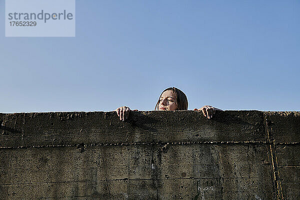 Junge Frau schaut über Betonwand