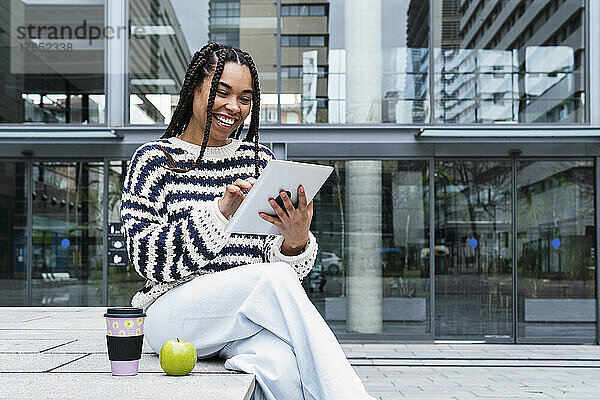 Fröhliche junge Geschäftsfrau mit Tablet-PC sitzt im Büropark