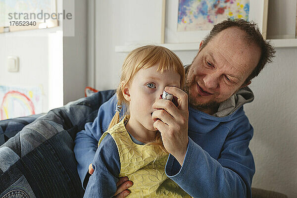 Vater hilft seiner Tochter  die zu Hause einen Asthmainhalator benutzt