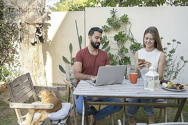 Lächelndes Paar mit Laptop und Smartphone sitzt im Hinterhof