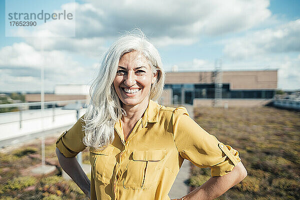 Glückliche Geschäftsfrau mit grauen Haaren im Büropark an einem sonnigen Tag