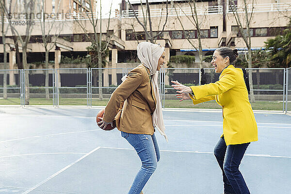 Fröhliche Geschäftsfrauen spielen Basketball auf dem Sportplatz