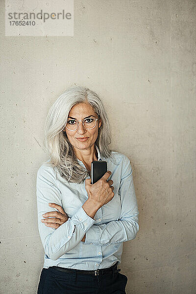 Geschäftsfrau mit Brille hält Smartphone vor Wand