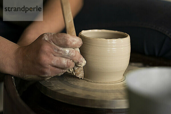 Frau mit Handwerkzeug formt Tontopf in Werkstatt