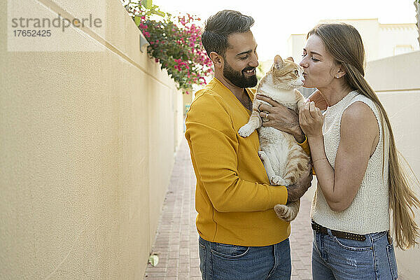 Smiling man looking at woman kissing cat in alley