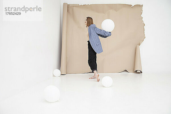 Junge Frau balanciert Ballon auf Händen vor braunem Hintergrund