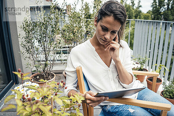 Frau blickt auf einen Tablet-PC  der auf einem Stuhl auf dem Balkon sitzt