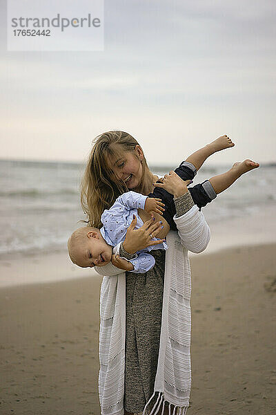 Glückliche Mutter trägt Sohn am Strand bei Sonnenuntergang