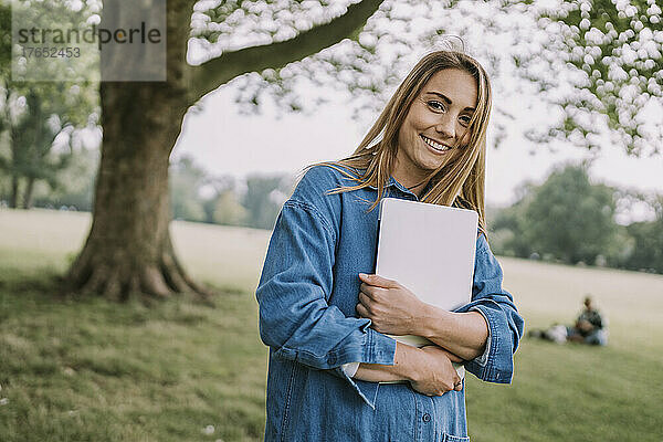 Lächelnde schöne Frau mit Laptop steht im Park