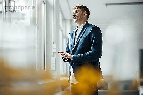 Lächelnder Geschäftsmann  der im Büro durch das Fenster schaut